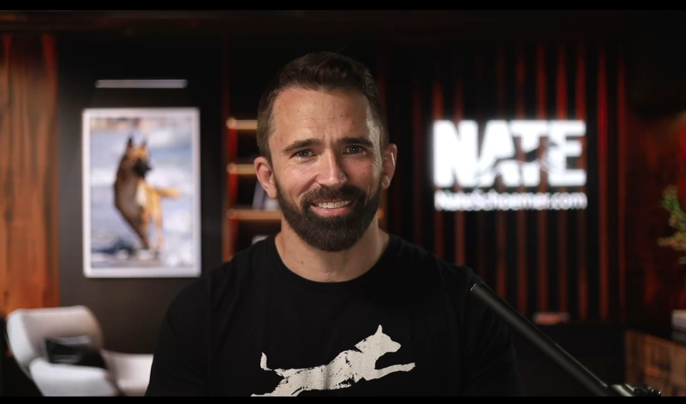 Nate Schoemer during a virtual training session, seated with a confident smile in a professional studio setup.